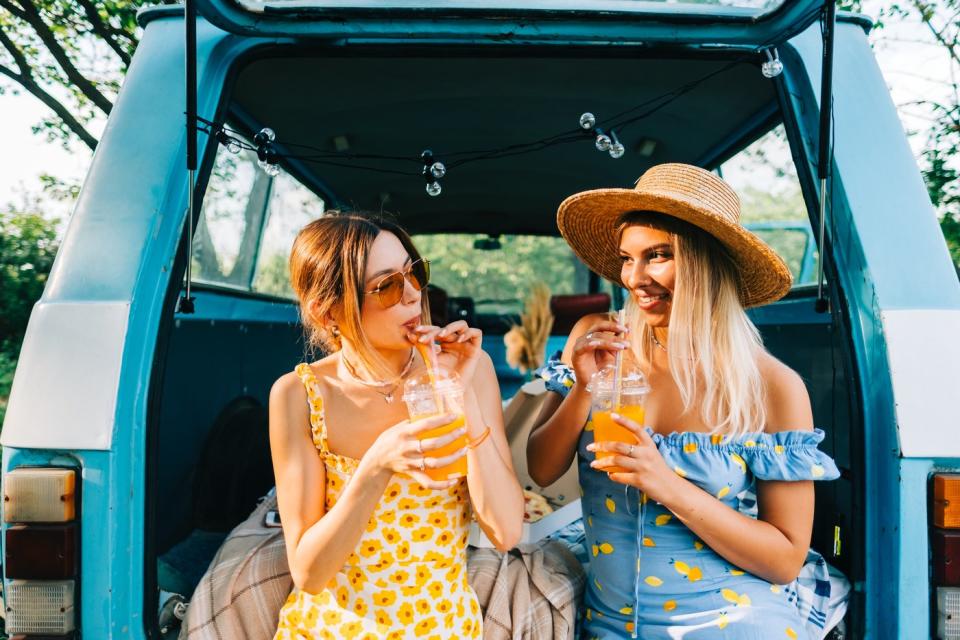 Two friends drink lemonade in the back of a van.