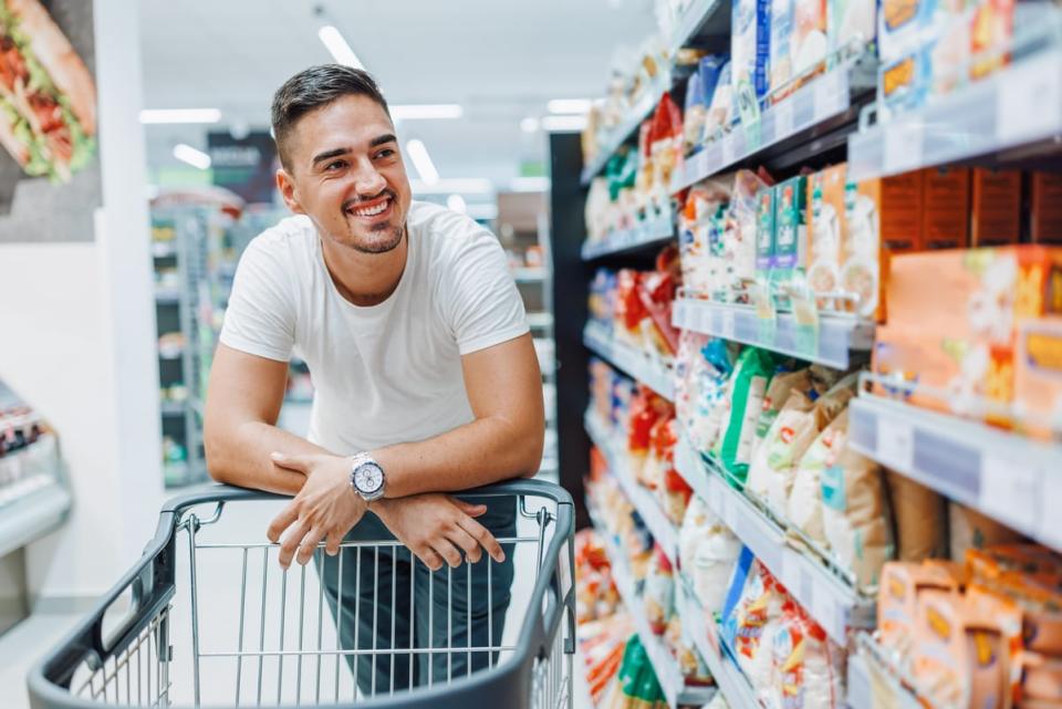 A person smiling while pushing a shopping cart through a store in a snack aisle. 