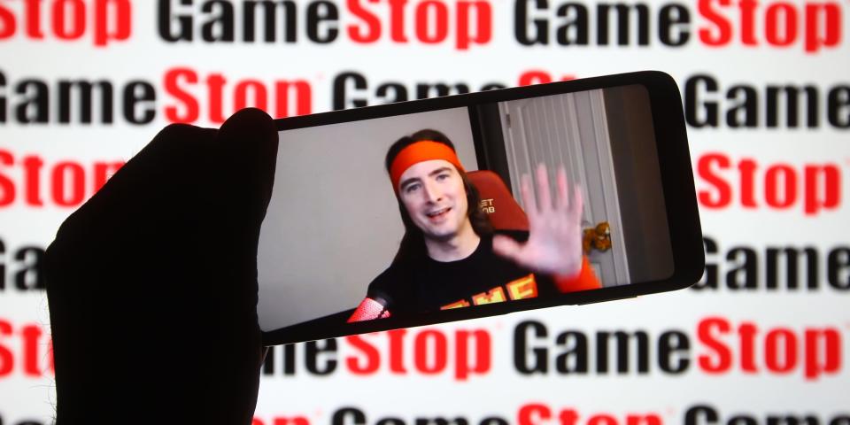 A video of Keith Gill being played on a smartphone in front of a background of GameStop logos.