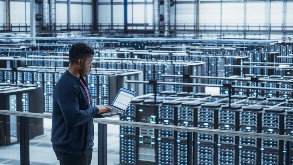 A man on a laptop in a server room.