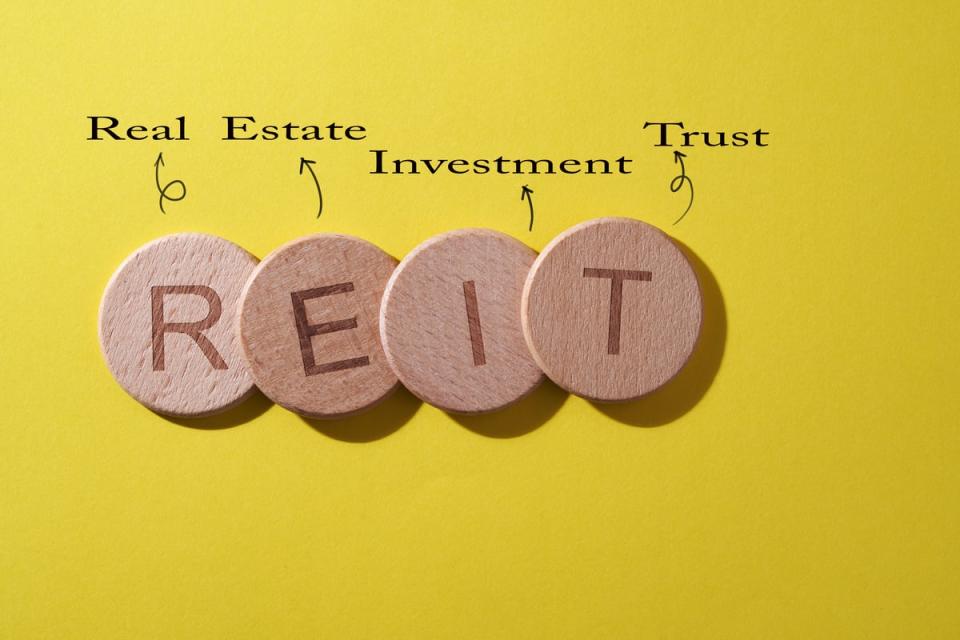 Wooden coins spelling out REIT with words above explaining the acronym.