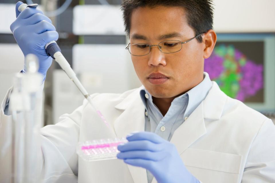 A lab technician using a pipette device to place liquid samples on a test tray.